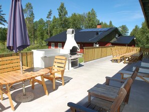 An outdoor patio with wooden furniture, a barbecue grill, and a house with a dark roof in the background. - Holiday Home in Mellerud (Mellerud)
