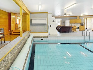 A swimming pool with tiled flooring, wooden walls, a kitchen area with cabinets, and a seating area with a sofa. - Holiday Home in Mellerud (Mellerud)