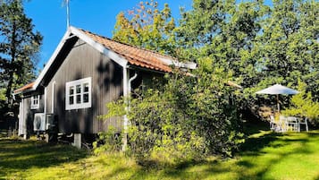 Una cabaña de madera con techo inclinado, rodeada de abundante vegetación y árboles.