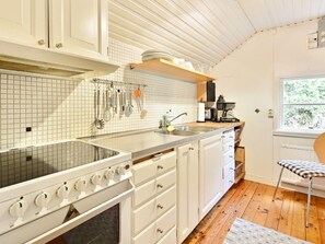 Een keuken met witte kasten, een roestvrijstalen spoelbak en een raam met uitzicht op groen.