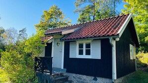 A small, single-story wooden cabin with a tiled roof, a front porch, and a stone foundation. - Holiday Home in Hallabro (Hallaröd)