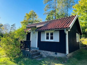 A small, single-story wooden cabin with a tiled roof, a front porch, and a stone foundation. - Holiday Home in Hallabro (Hallaröd)