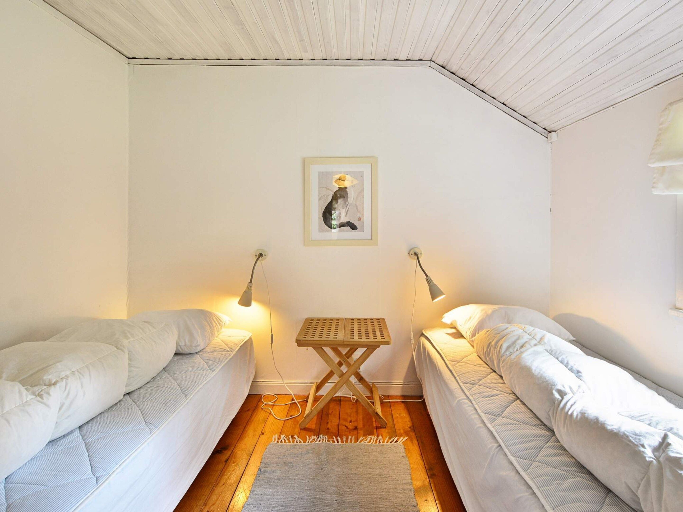 A room with two single beds, a small wooden table, and two wall-mounted lamps.