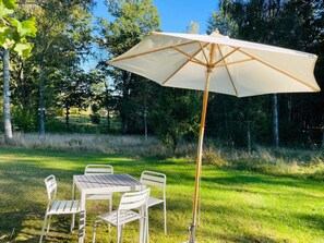 An outdoor dining area with a table and chairs, a large umbrella, and a natural backdrop of trees. - Holiday Home in Hallabro (Hallaröd)