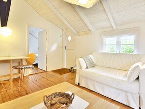 Een gezellige kamer met een witte bank, een eettafel met een stoel, en een raam met uitzicht op groen.