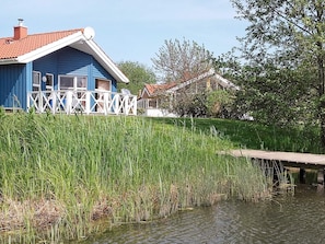 A blue house with a white fence and a dock extending into a body of water.
