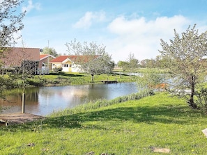 A serene lakeside setting with a wooden dock, a small bridge, and houses with red-tiled roofs. - Holiday Home in Otterndorf (Otterndorf)