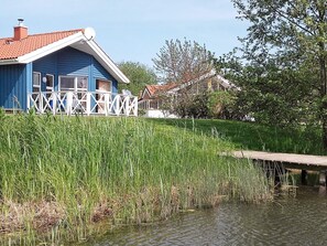 A blue house with a white fence and a dock extending into a body of water. - Holiday Home in Otterndorf (Otterndorf)