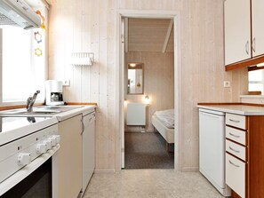 Cocina compacta con lavabo, cafetera y estufa. Un acceso da a un dormitorio con cama y radiador.