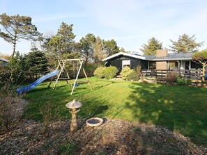 A residential property with a grassy yard, a swing set, a bird bath, and a house with a porch.