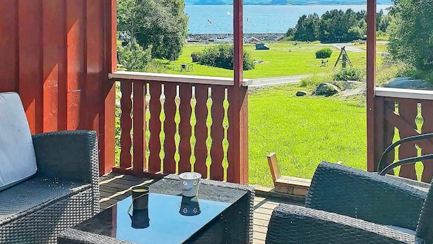 Ein Balkon mit Korbmöbeln, einem Glastisch und Blick auf einen See und Grünflächen.