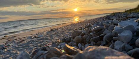 Una playa con piedras y un atardecer al fondo.