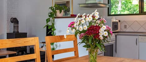A wooden dining table with a vase of flowers, chairs, a stove, and a window with a view of trees.