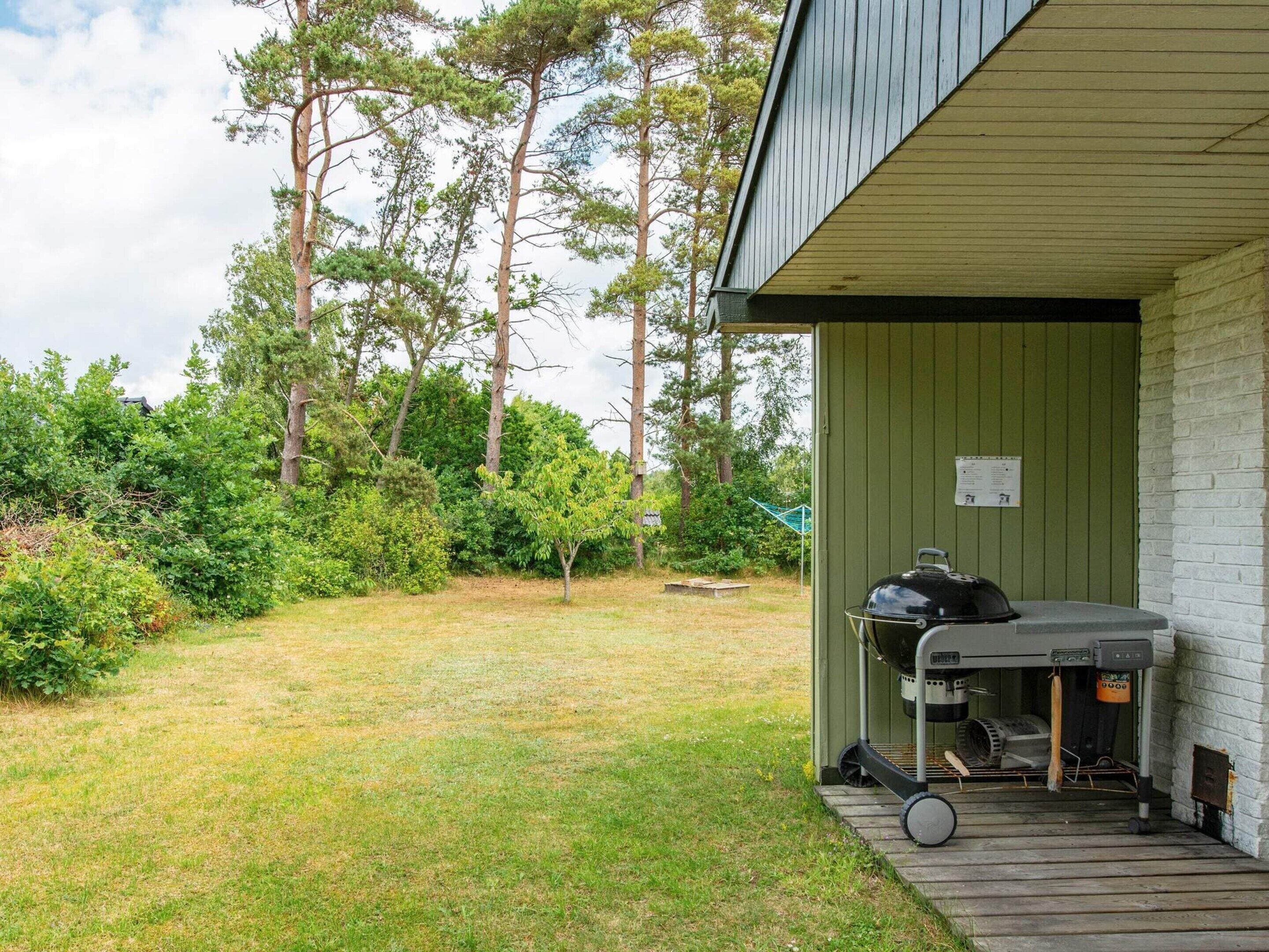 Et overdækket udendørsområde med grill og træterrasse.