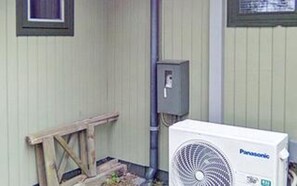 A white Panasonic air conditioner unit outside a building with a metal utility box and a wooden structure nearby.