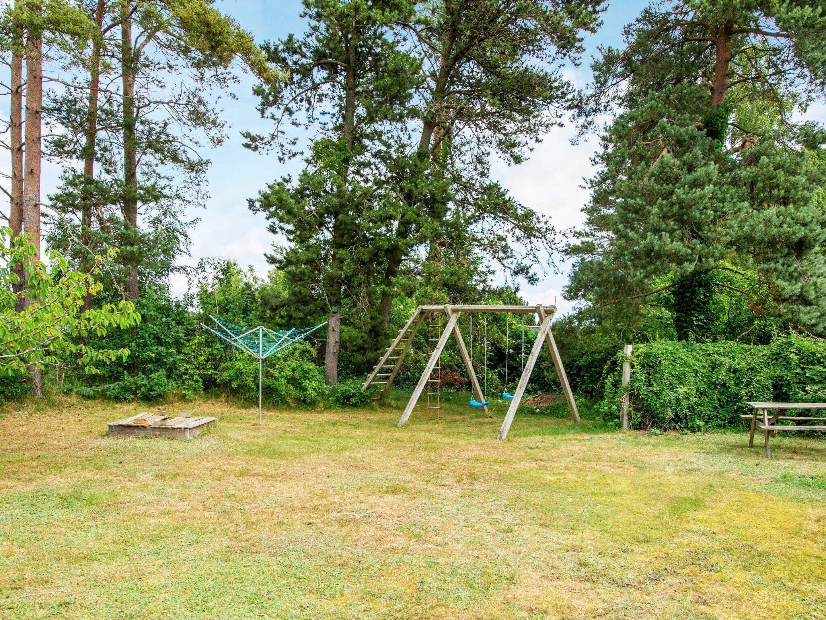 Un parque infantil con columpios y una estructura para escalar en un área boscosa.