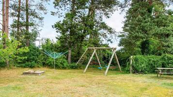 Un parque infantil con columpios y una estructura para escalar en un área boscosa.