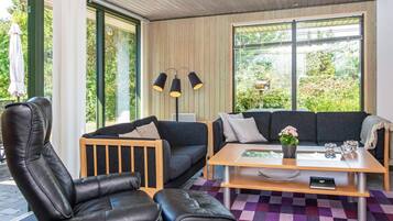 Una sala de estar moderna con un sofá, dos sillones de cuero, una mesa de centro y ventanas amplias que ofrecen vistas a zonas verdes.