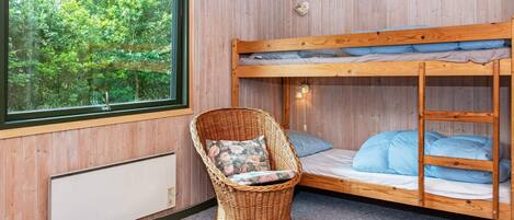 A bunk bed with a view of greenery outside, a wicker chair with cushions, and a wall-mounted light fixture.
