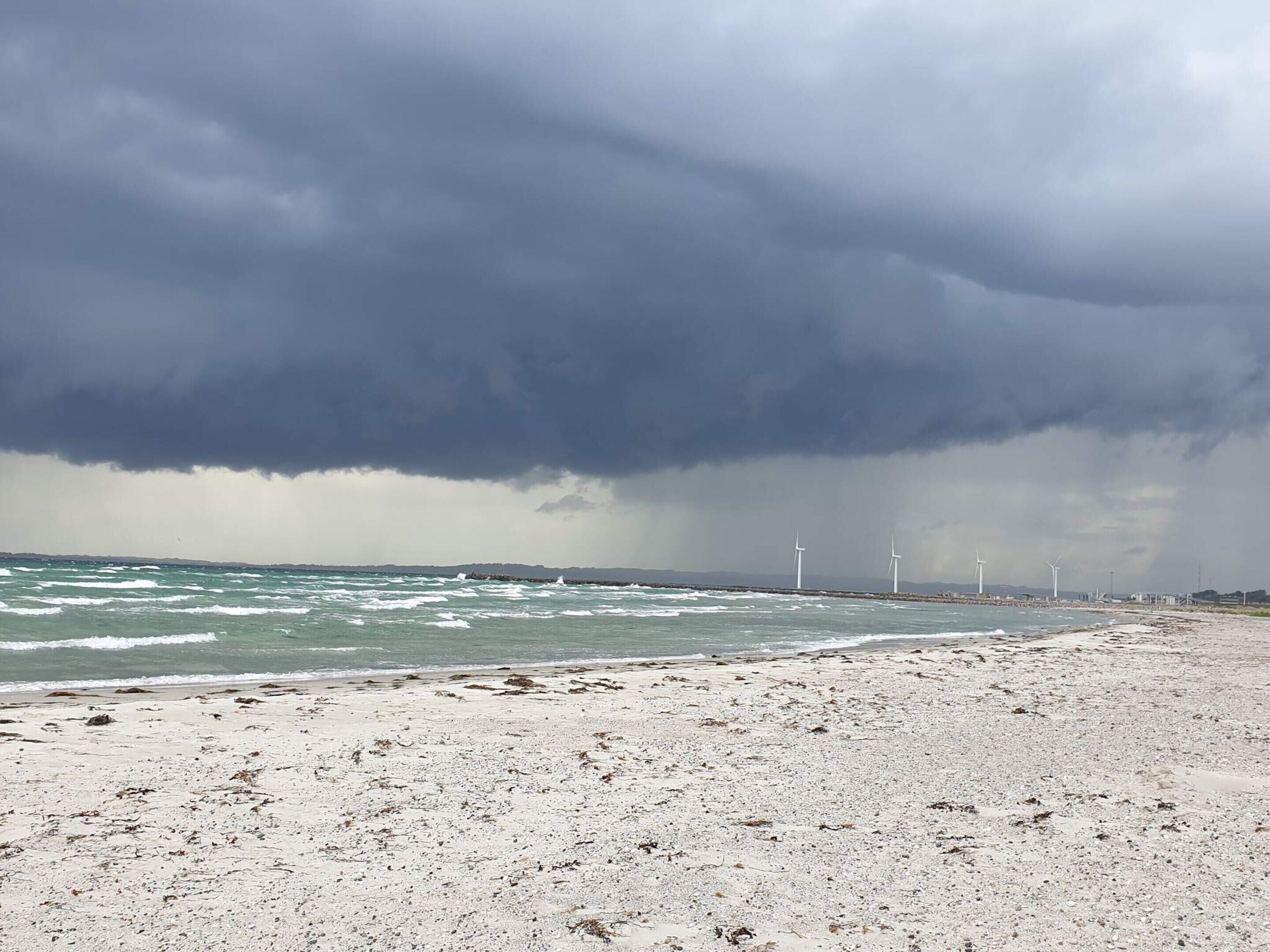Ein Strand mit Windkraftanlagen in der Ferne unter einem stürmischen Himmel.