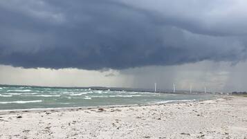 En strand med vindmøller i det fjerne under en stormfuld himmel.