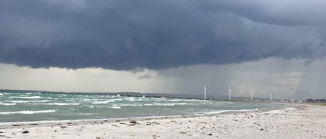 A beach with wind turbines in the distance under a stormy sky.