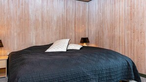 Une chambre avec un plafond en pente en bois, un lit recouvert d’une courtepointe sombre à motifs, deux lampes de chevet et une table de chevet avec une lampe.
