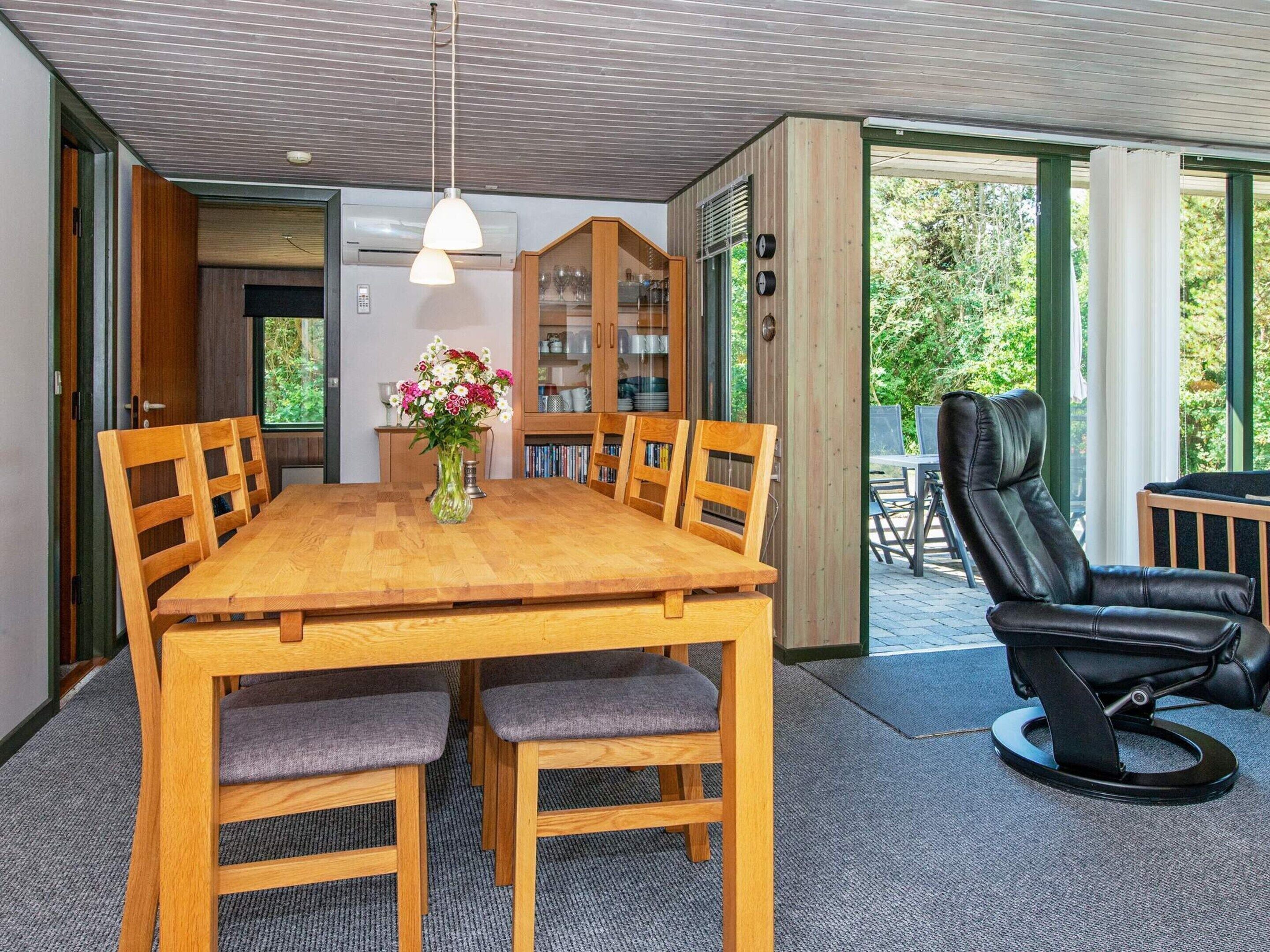 Un comedor con mesa y sillas de madera, un florero con flores y una silla de cuero negro.