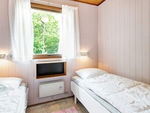 A bedroom with two beds, a window with curtains, a wall-mounted heater, and a view of greenery outside. - 4 Star Holiday Home in Aakirkeby (Akirkeby)