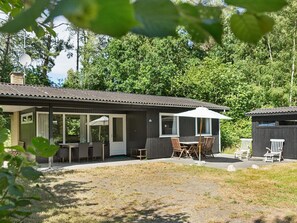 A single-story building with a covered patio area, a dining table with chairs, and a small outdoor seating area with additional chairs. - 4 Star Holiday Home in Aakirkeby (Akirkeby)