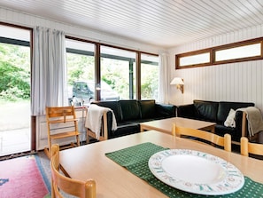 A room with a wooden table, chairs, a sofa, and a window with a view of greenery.