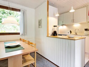 A compact kitchen with a dining area, featuring a wooden table, chairs, a white countertop, and a hanging light fixture.