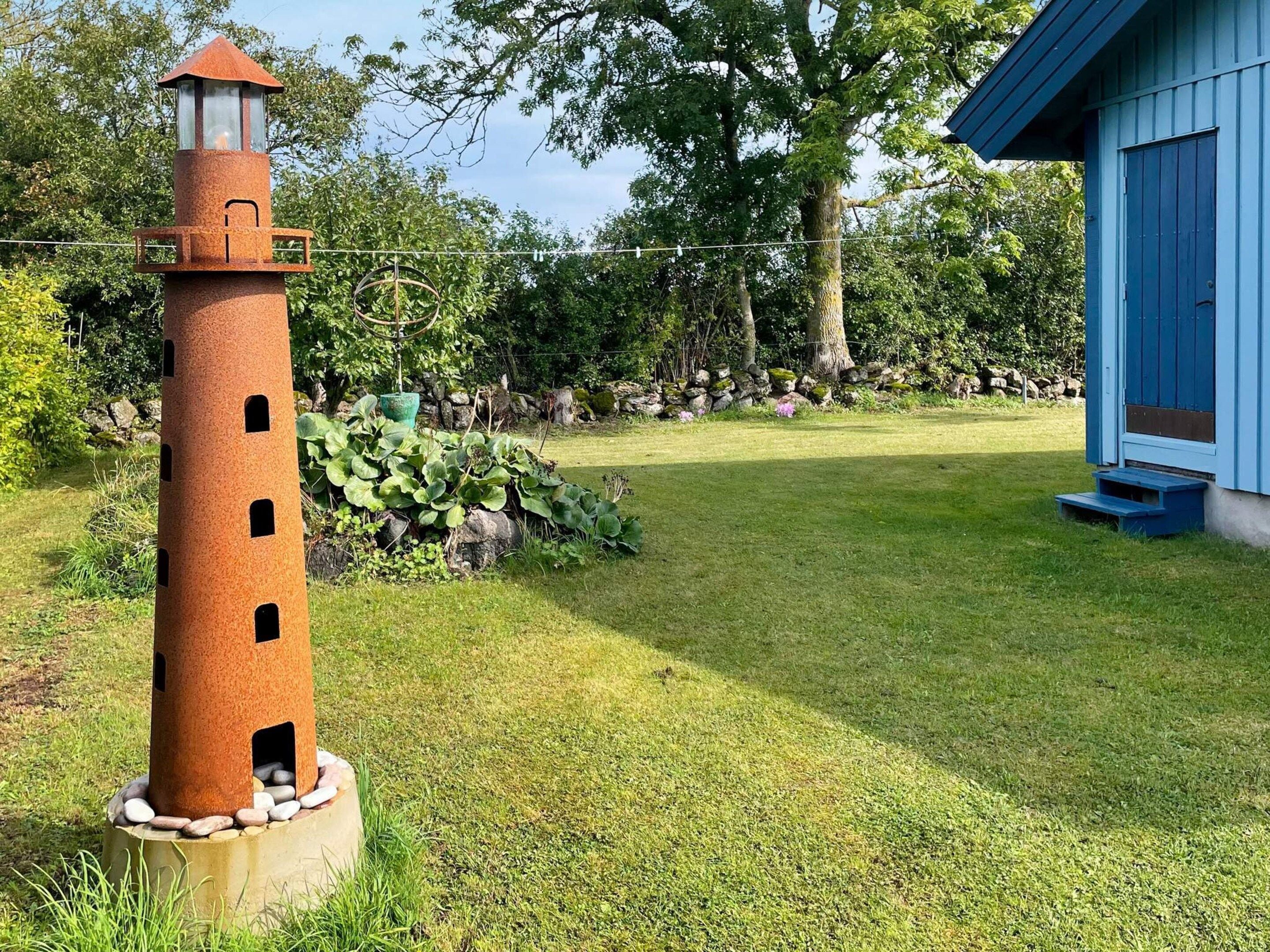 Ein Leuchtturm mit zylindrischem Unterteil und spitzem Turm, umgeben von einer Rasenfläche und einer Steinmauer.