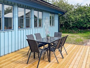 En blå byggnad med stora fönster och en terrass med ett bord och stolar.