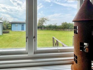 A view through a window with a grassy yard, a blue shed, and a metal structure. - 6 Person Holiday Home in Kopingsvik (Kopingsvik)