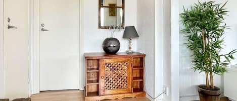 A wooden console table with a decorative vase and a lamp, a potted plant, a fire extinguisher, and a door with a mirror above it.
