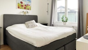 A neatly made bed with a grey headboard, a pillow with text, a small bedside table, and a window with curtains. - 6 Person Holiday Home in Kopingsvik (Kopingsvik)