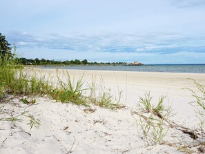 A beach with white sand, sparse vegetation, and a distant pier. - 6 Person Holiday Home in Kopingsvik (Kopingsvik)