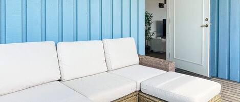 Un canapé d’angle blanc est placé contre un mur bleu, près d’une porte et d’une fenêtre.