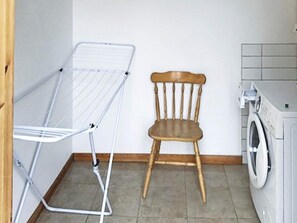 A laundry area with a drying rack, a wooden chair, and a washing machine. - Holiday Home in Uddevalla (Uddevalla)