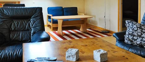 A cozy living room with a sloped ceiling, a sofa, a coffee table with remote controls, and a painting on the wall.