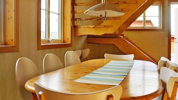 A wooden dining table with chairs, a striped placemat, and a hanging light fixture in a room with wooden walls and a visible staircase.