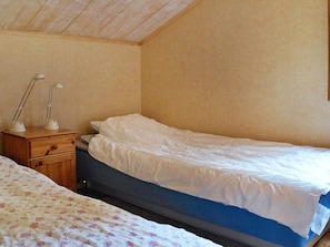 Un dormitorio con una cama individual, una mesita de noche con dos lámparas y una colcha estampada con motivos florales.