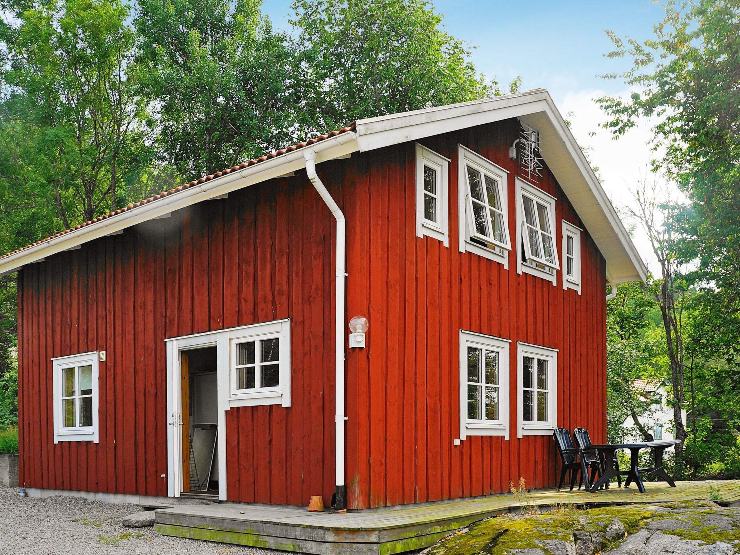 Een rood houten gebouw met een witte deur en ramen, een klein terras met buitenmeubels, en een heldere lucht.
