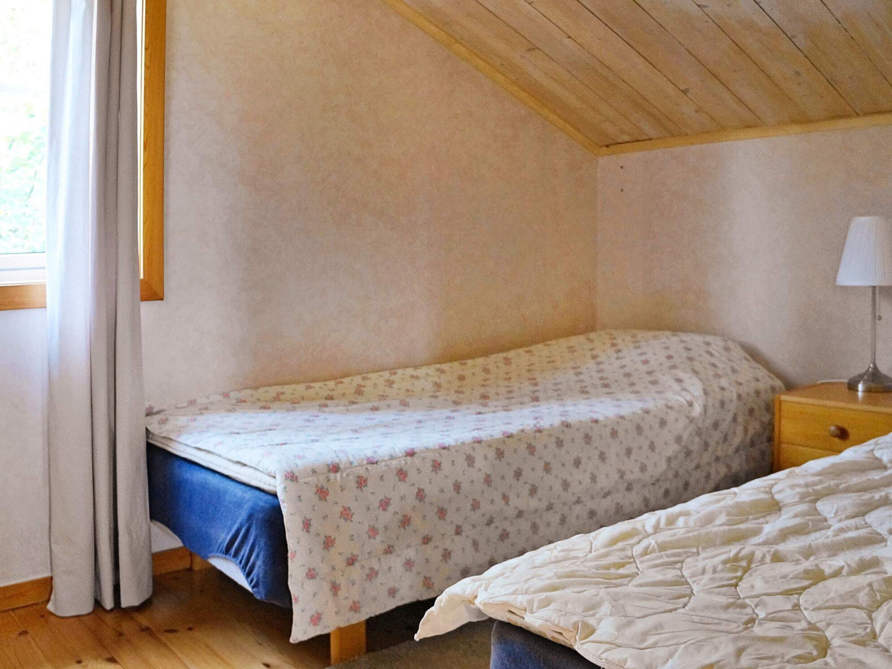A bedroom with a single bed, a nightstand with a lamp, and a window with curtains.