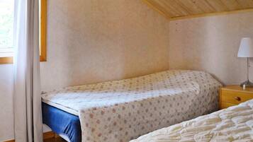 A bedroom with a single bed, a nightstand with a lamp, and a window with curtains.