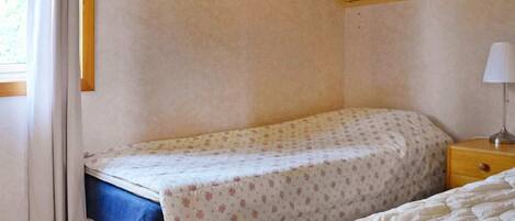 A bedroom with a single bed, a nightstand with a lamp, and a window with curtains.