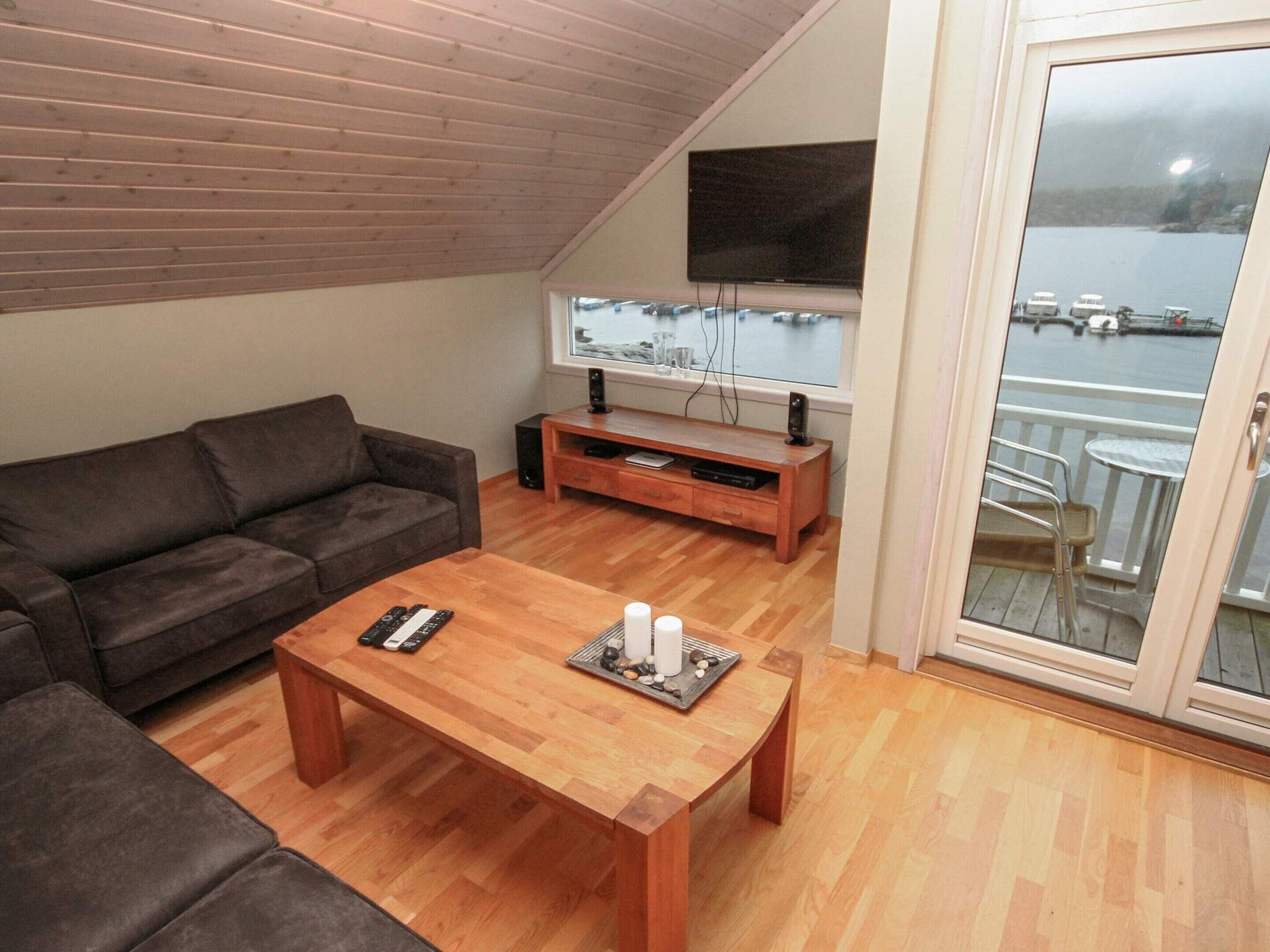 A cozy living room with a wooden ceiling, a brown sofa, a wooden coffee table, and a TV on the wall.