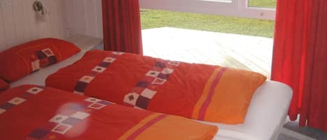 Una cama doble con colcha y almohadas estampadas, una ventana con cortinas rojas y vista a un cuerpo de agua.