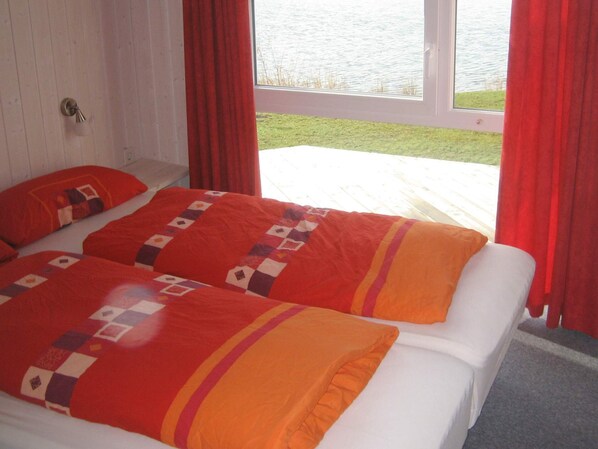 Una cama doble con colcha y almohadas estampadas, una ventana con cortinas rojas y vista a un cuerpo de agua.